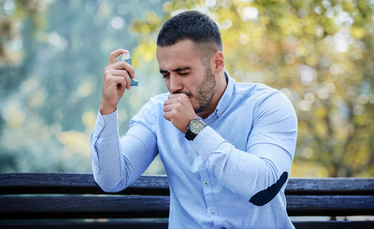 Man coughing while using his inhaler on a bench
