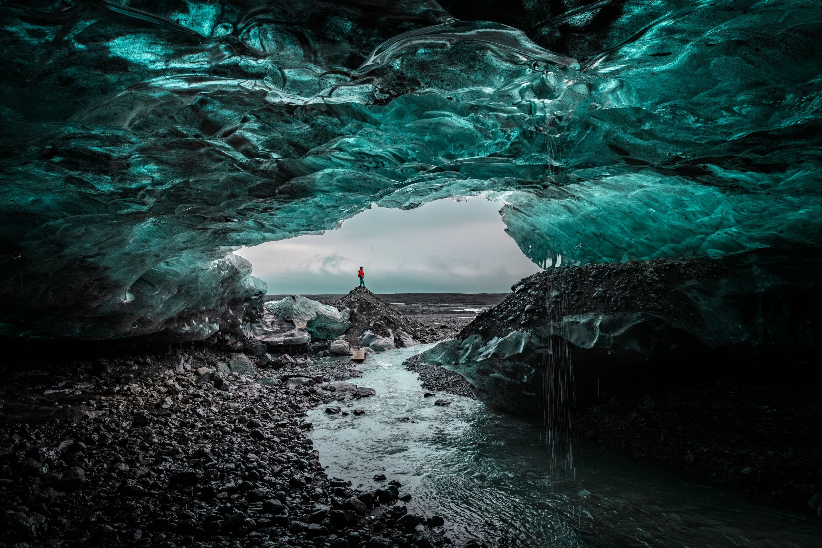 A person standing at the mouth of a blue ice cave in Iceland