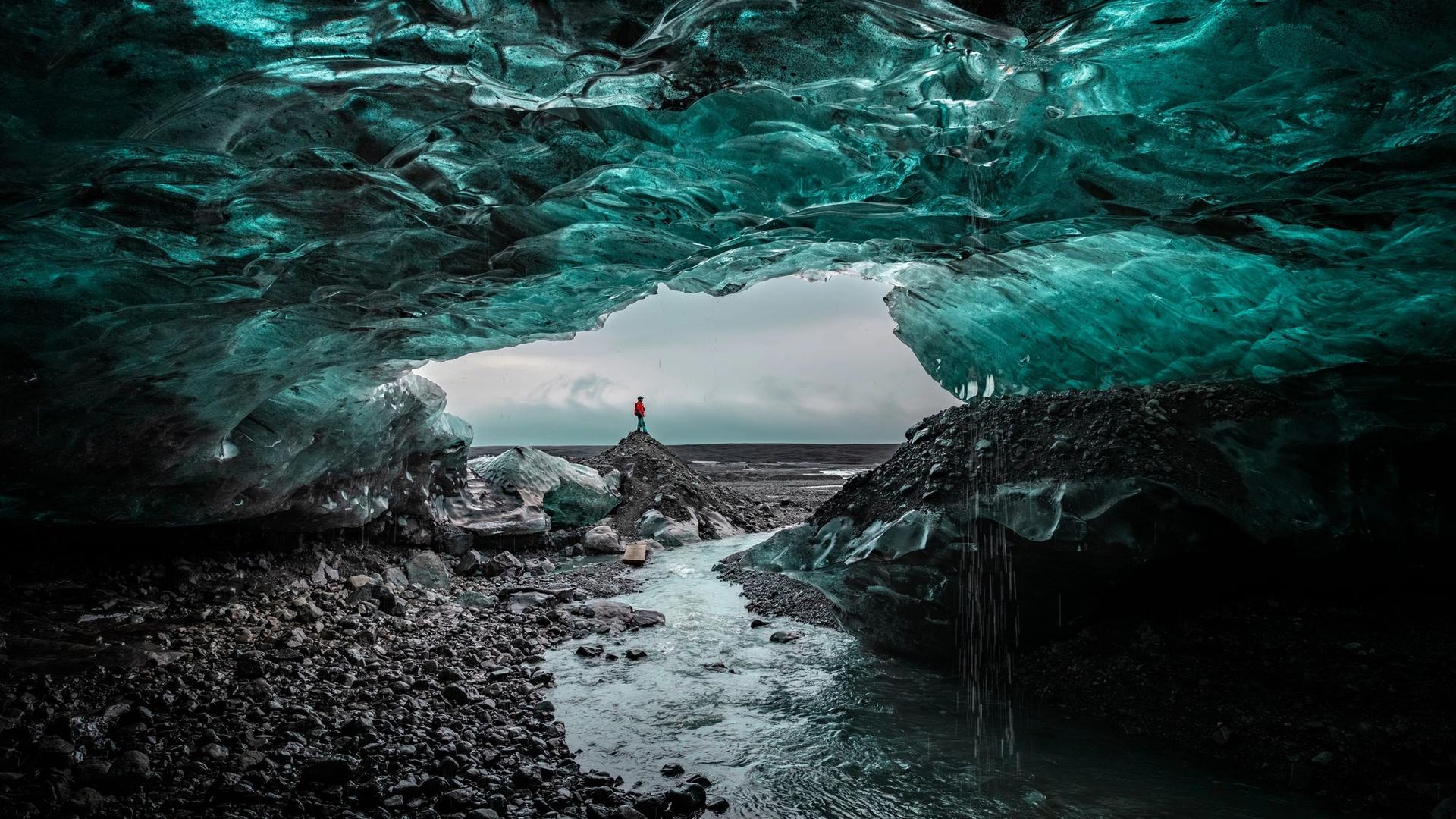 A person standing at the mouth of a blue ice cave in Iceland