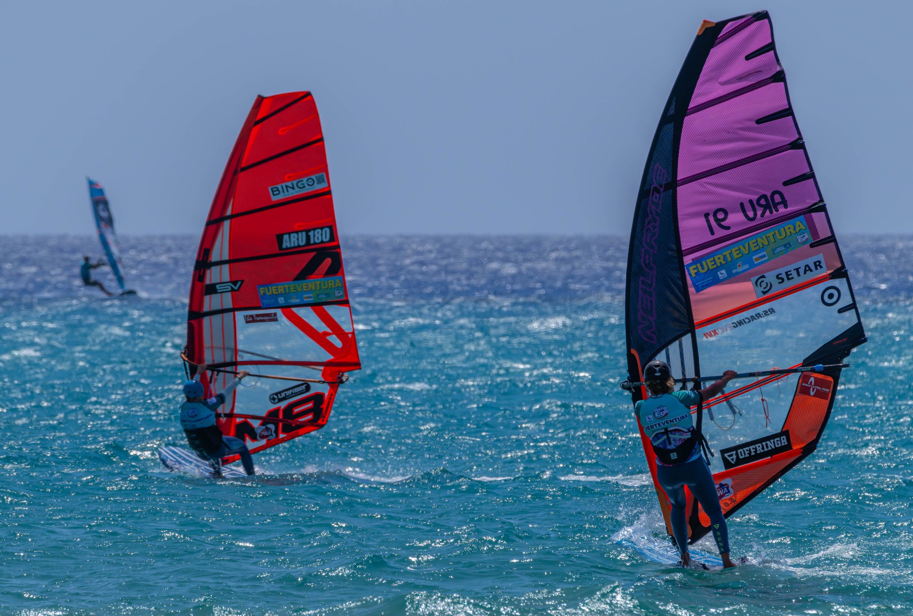 Windsurfers on turquoise water off Fuerteventura, their sails marked with the island's name