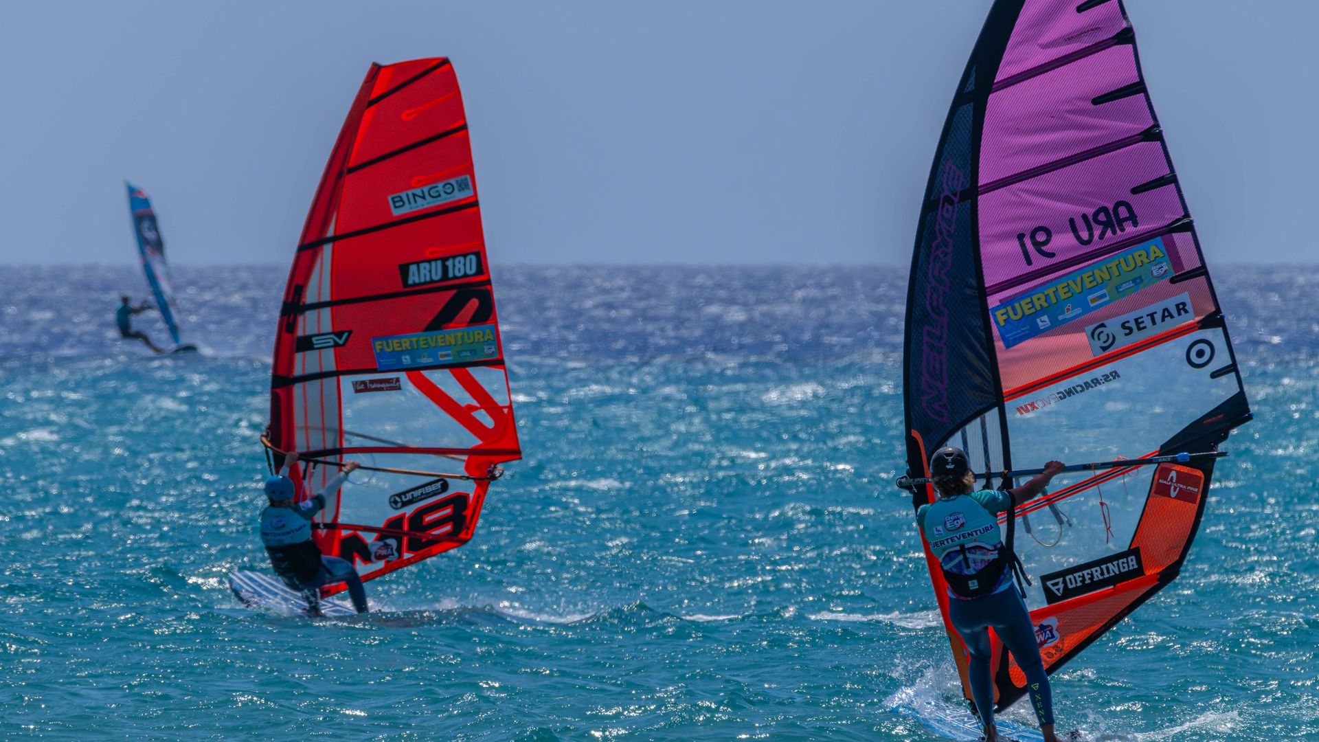 Windsurfers on turquoise water off Fuerteventura, their sails marked with the island's name