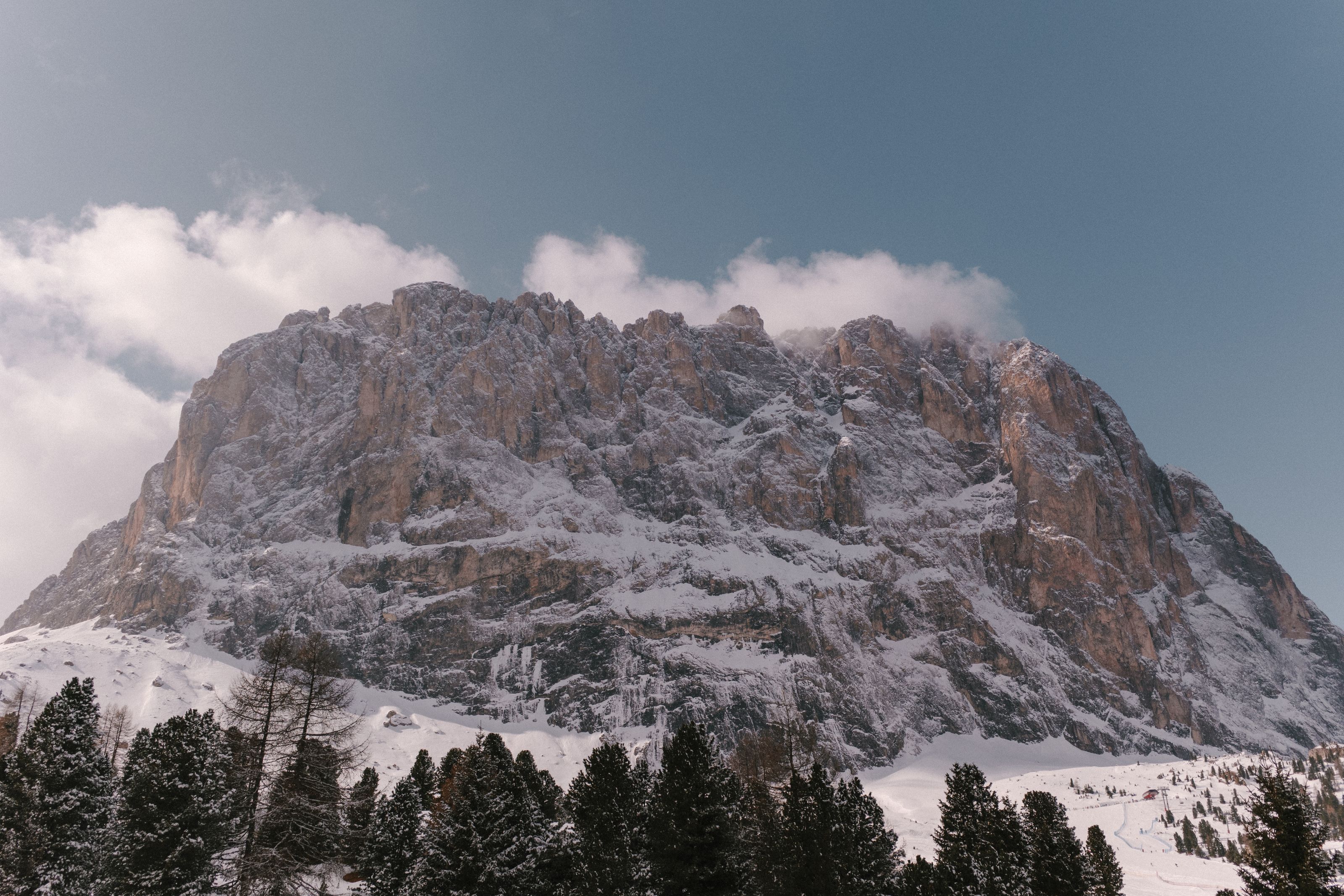 Snow on the rock walls of Sassolungo above the pine forest of Val Gardena