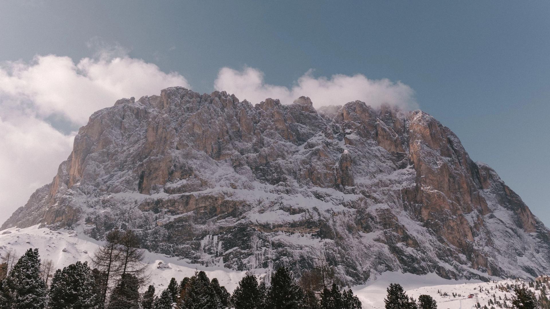 Snow on the rock walls of Sassolungo above the pine forest of Val Gardena