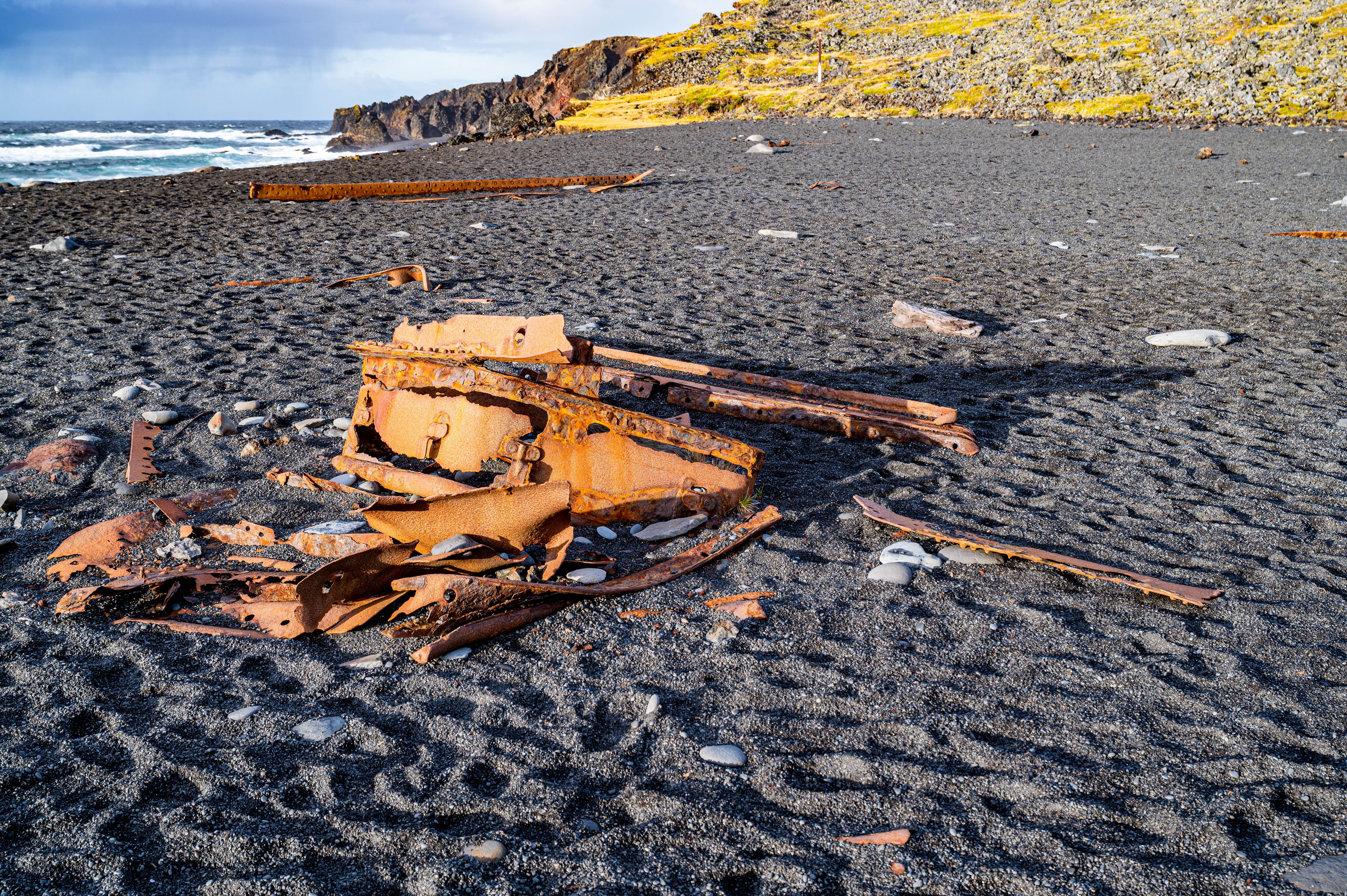 Black pebble beach with rusted shipwreck fragments scattered on the shore