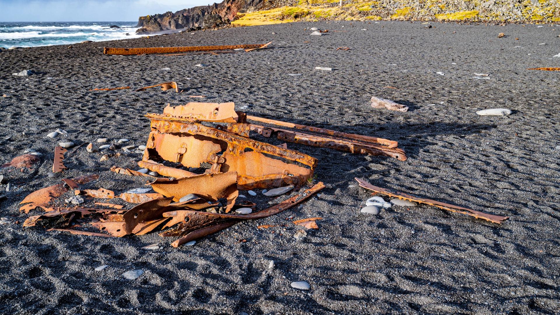 Black pebble beach with rusted shipwreck fragments scattered on the shore