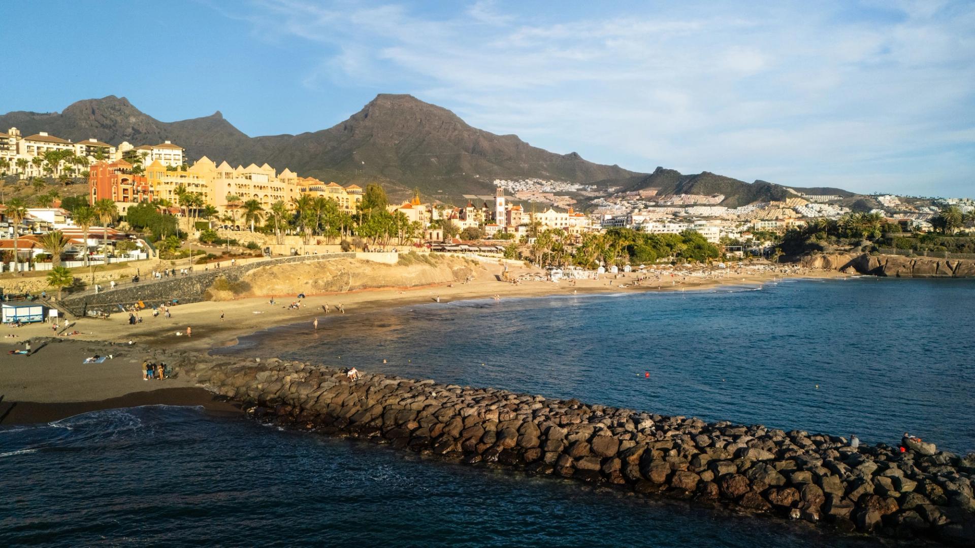 A beach on Costa Adeje below dry mountains, with hotels behind the sand