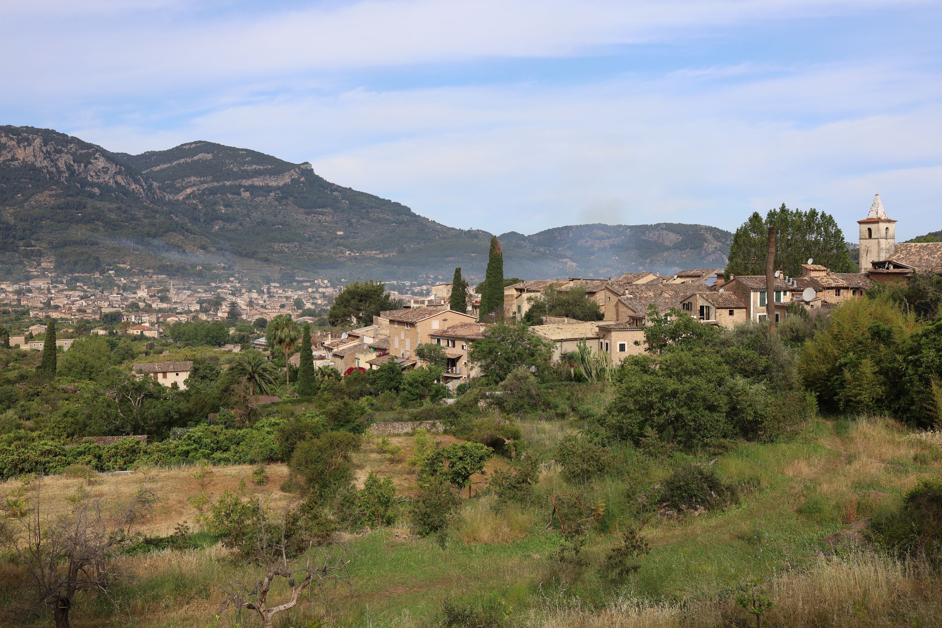The village of Biniaraix among green slopes, with the town of Sóller and the mountains behind