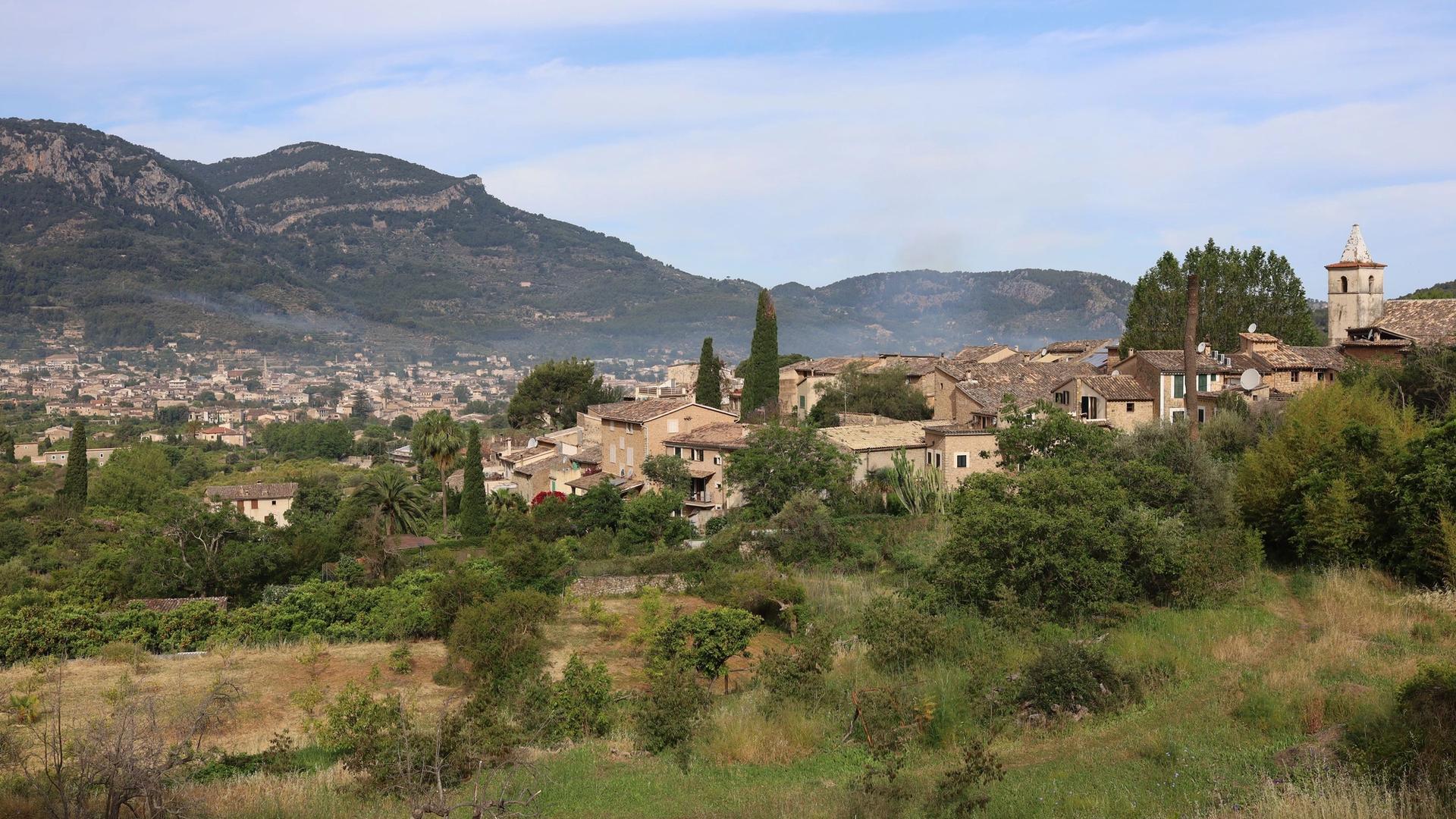 The village of Biniaraix among green slopes, with the town of Sóller and the mountains behind