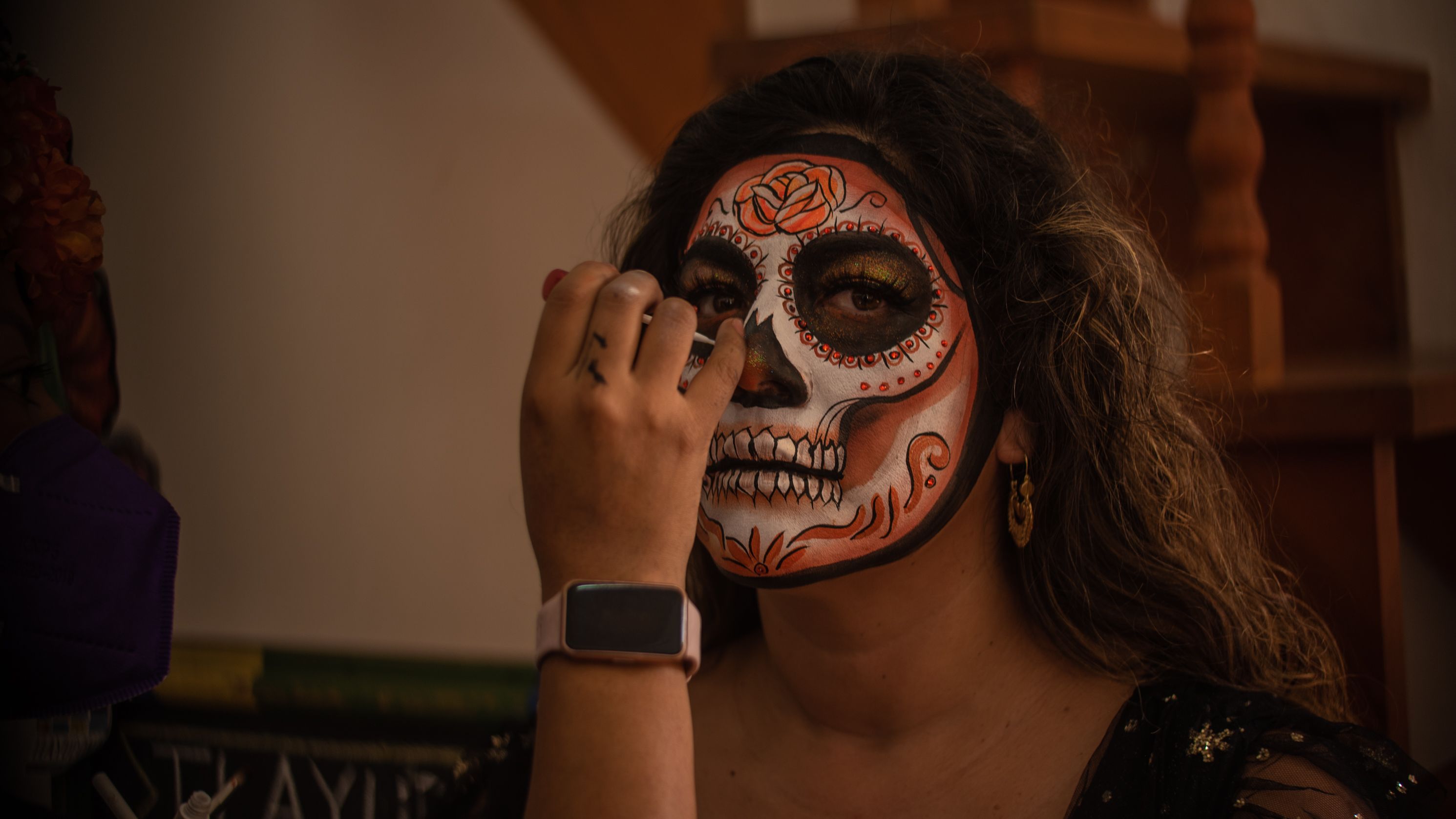 Una mujer recibe los últimos detalles de un elaborado maquillaje tradicional de catrina para el Día de Muertos en Oaxaca.  A woman is being shown the final touches of an elaborate traditional Catrina makeup look for the Day of the Dead in Oaxaca.