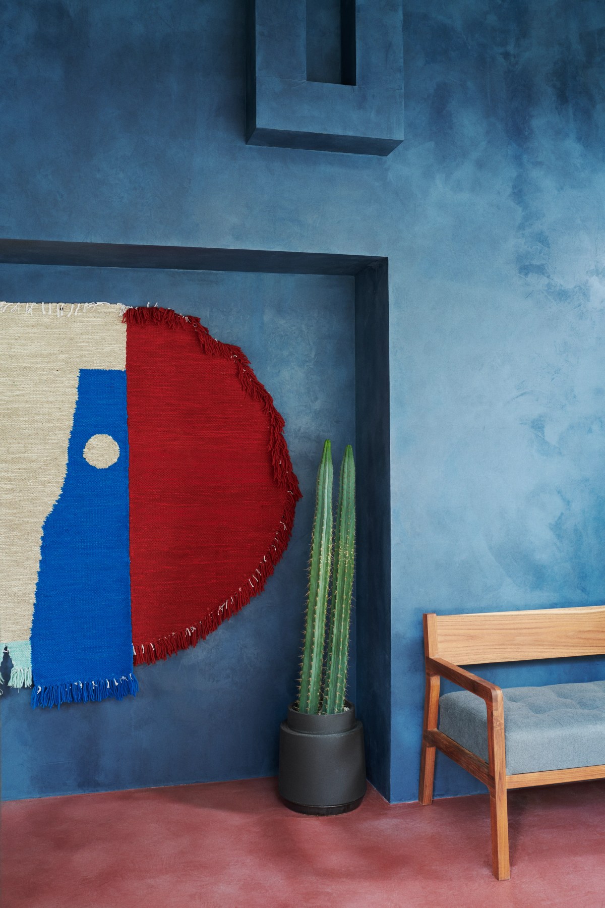 Blue walls, cactus, wall rug and wooden bench with grey upholstery