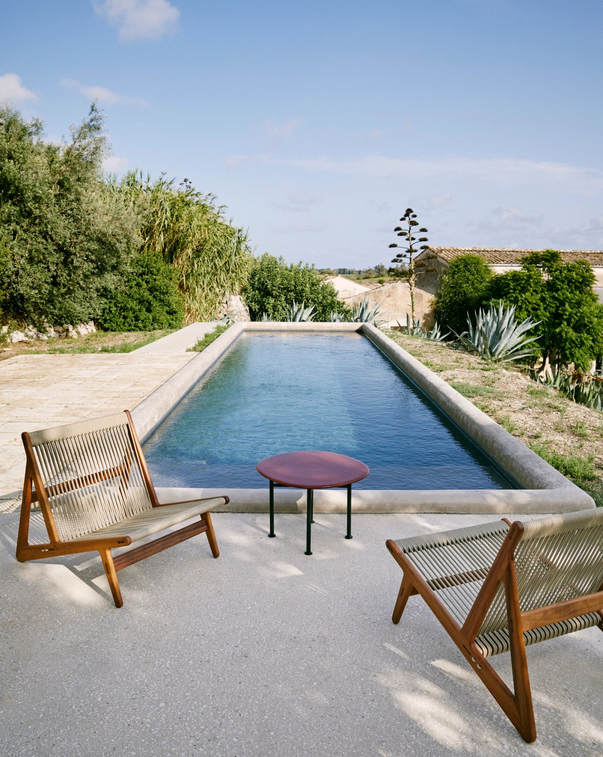 Red table with black legs and wooden deck chairs in front of a swimming pool