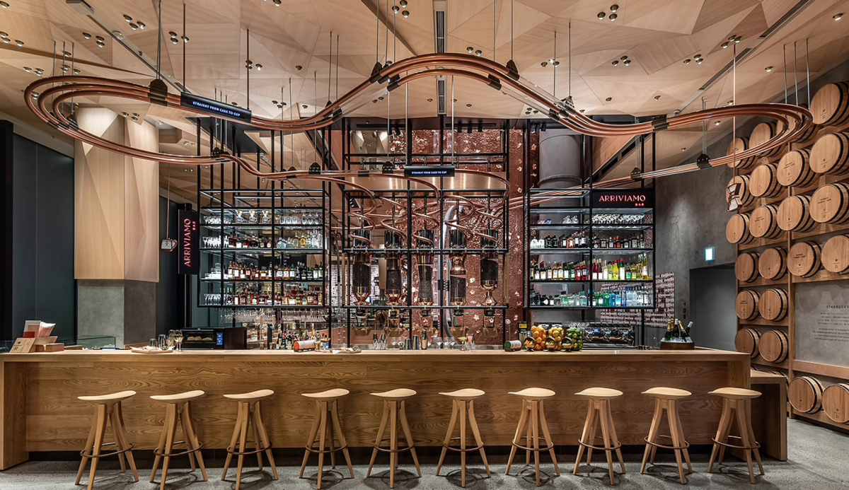Wooden bar stools in front of large bar with open shelving and brass piping in the ceiling
