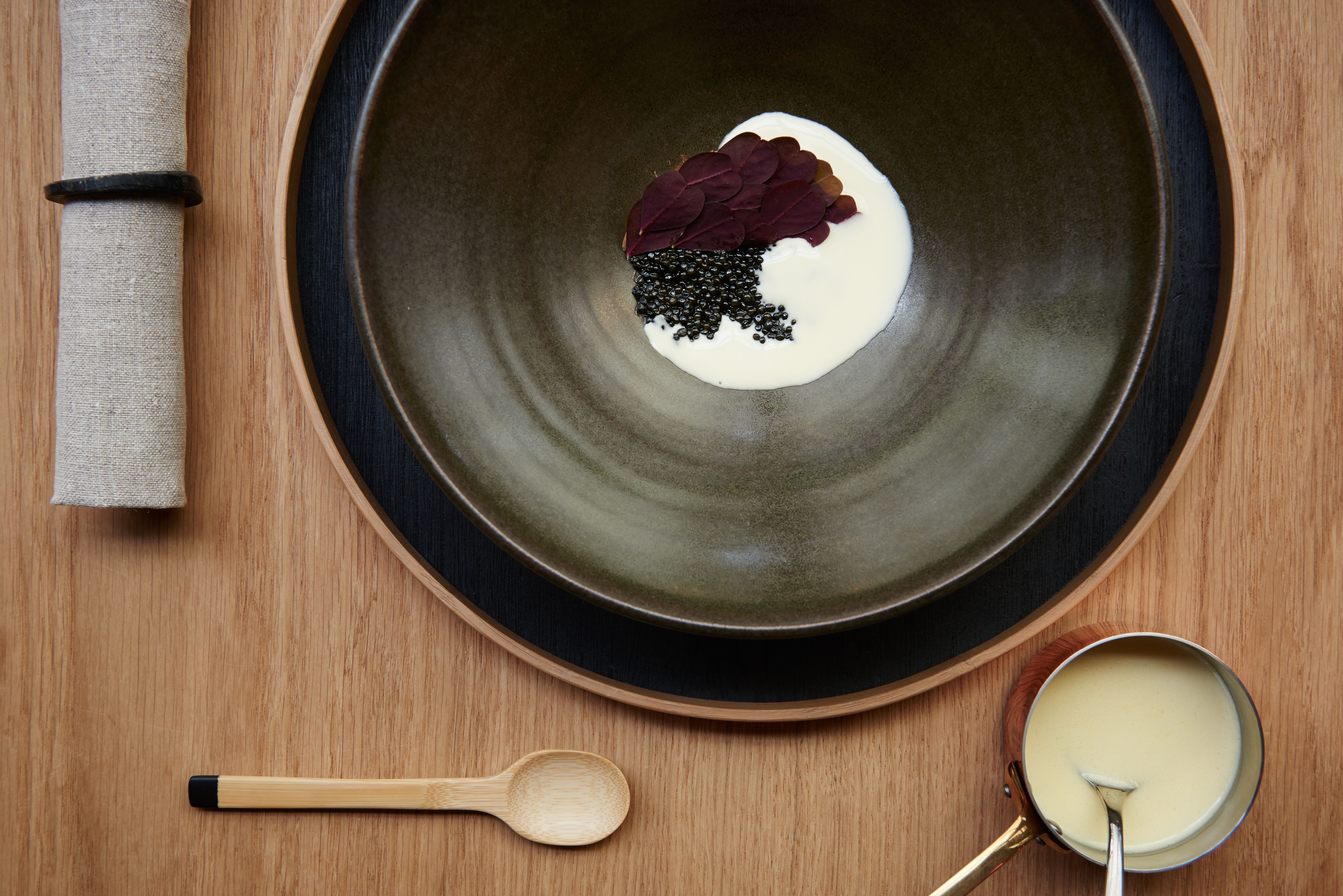 Bamboo spoon on wooden table next to dark plates in fine dining restaurant 