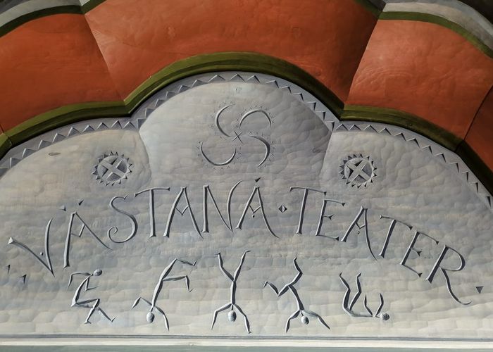 [:sv]Under det välvda krönet, partiet som kallas Tympanum, fyllde jag med hallingdansande streckfigurer och symboler från mitt mönsterbibliotek. Den kosmiska symbolen i mitten är inspirerat av ett mönster från en liten dragask på Gammelgården i Borlänge, en symbol som blivit en personlig favorit. För mig är den humanistisk evighetssymbol som kommunicerar livets kosmiska karusell, round and round we go, en rotation i all evighet.
Streckfigurer dansar Halling, en mönster-rapport i linje med Västanå Teaters kännemärke att blanda dans, musik, drama och, kostym, allt i en kokade folkkonstgryta.[:]