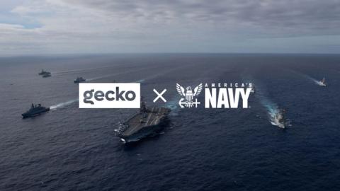 Gecko and U.S. Navy logos over an aircraft carrier group at sea