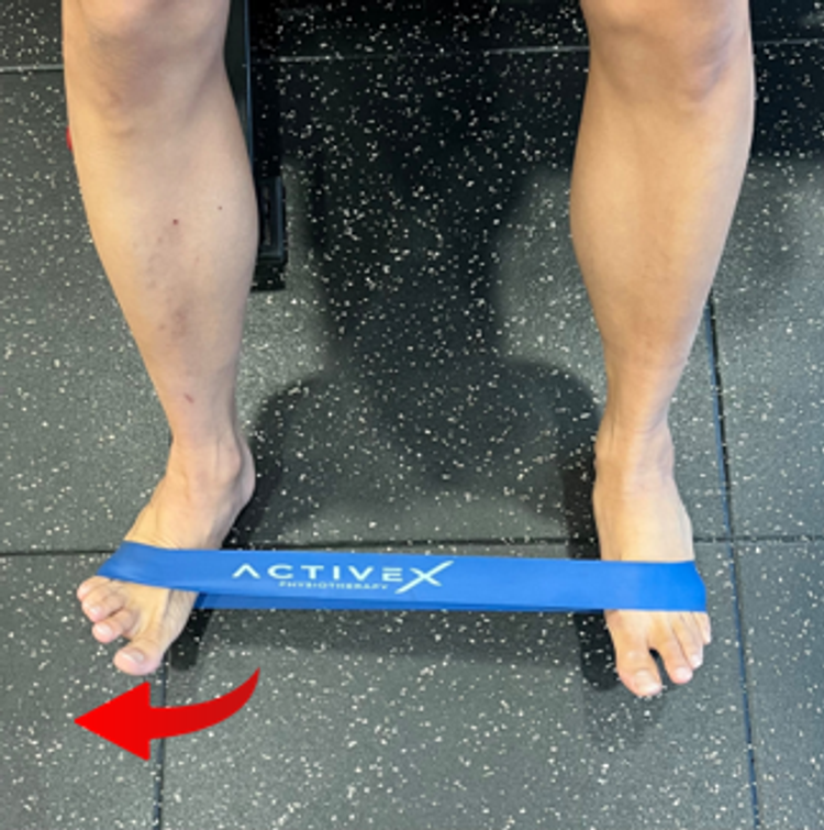 Seated banded ankle inversion and eversion strengthening drill. Red arrow moving in the direction of turning the foot outwards.