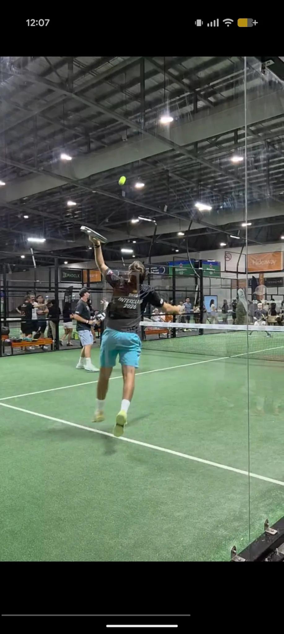 A player in an Interclub 2026 jersey leaps for an overhead smash during the Singapore Padel Interclub Cup 2026 on an indoor court.