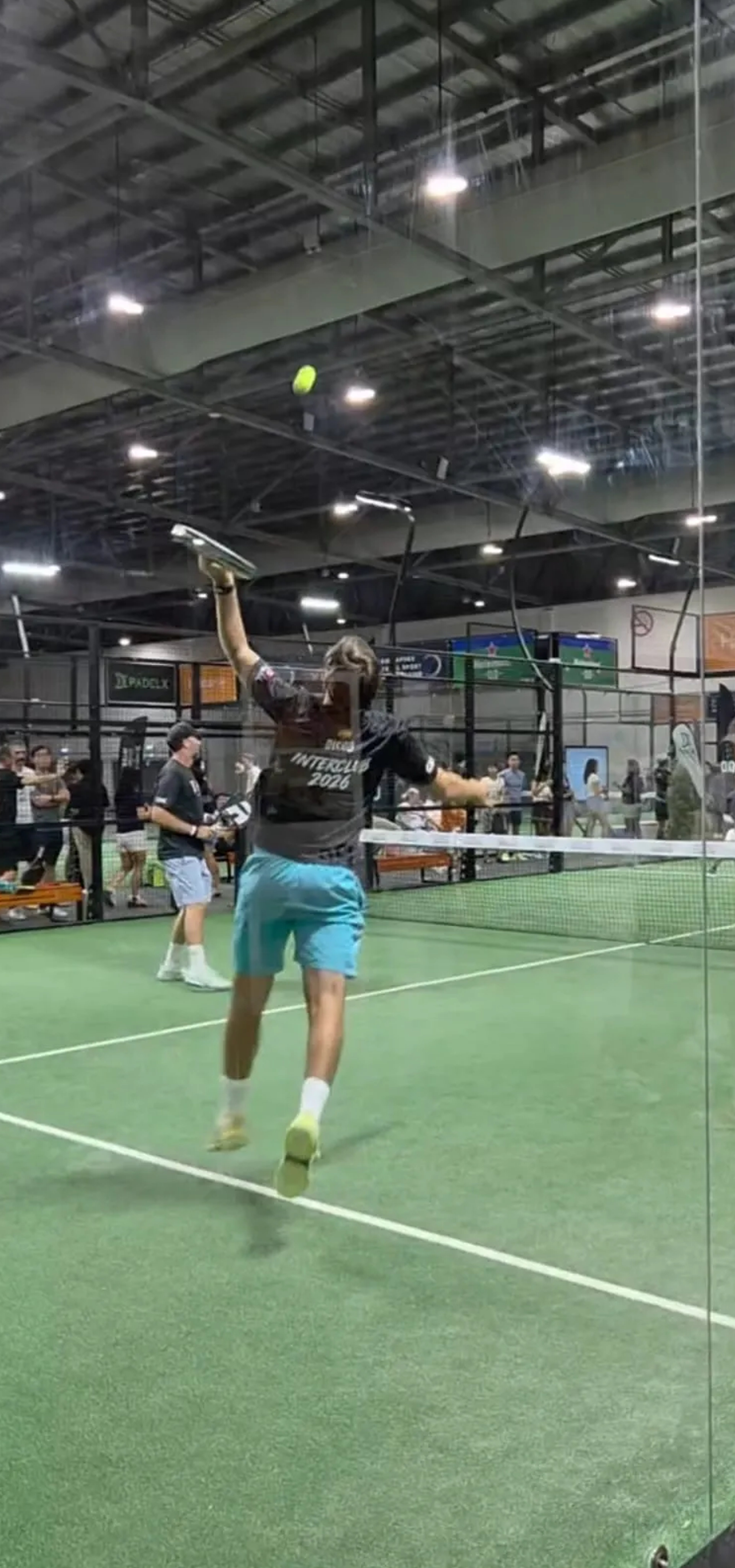 A player in an Interclub 2026 jersey leaps for an overhead smash during the Singapore Padel Interclub Cup 2026 on an indoor court.