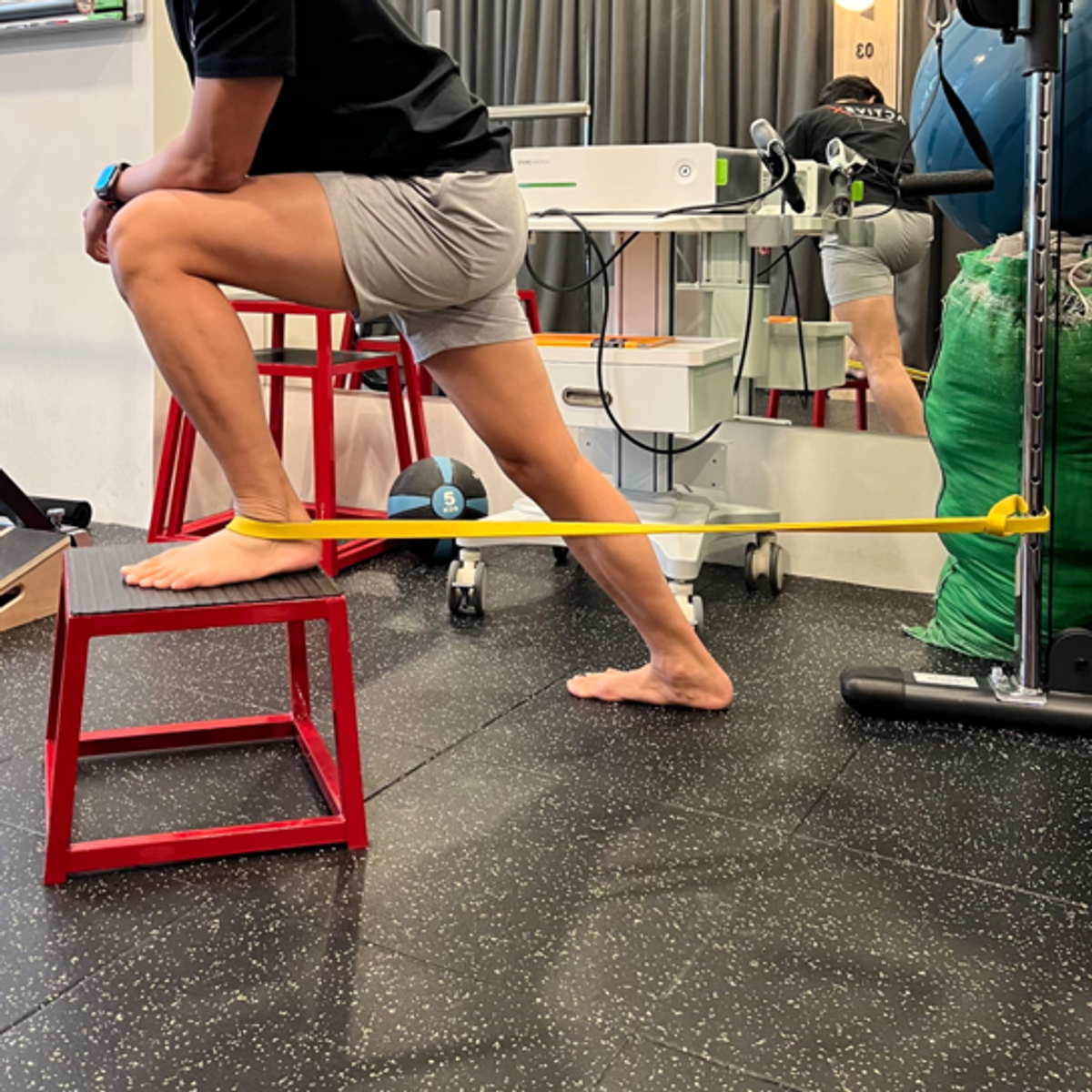 Physiotherapist Ivan performing banded ankle dorsiflexion in a half-kneeling position.