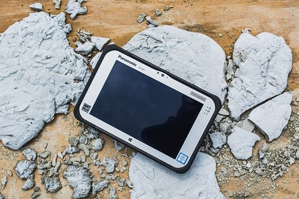Robuuste Panasonic Toughpad tablet op een houten ondergrond tussen brokken cement en gruis, geschikt voor gebruik op de bouwplaats.
