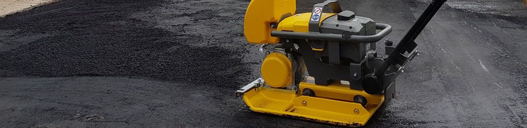 Trilplaatmachine in gebruik voor het verdichten van vers aangebracht reparatieasfalt op een wegdek. Laat me weten als je een alternatieve versie wilt voor SEO, productcatalogus of instructiedoeleinden.