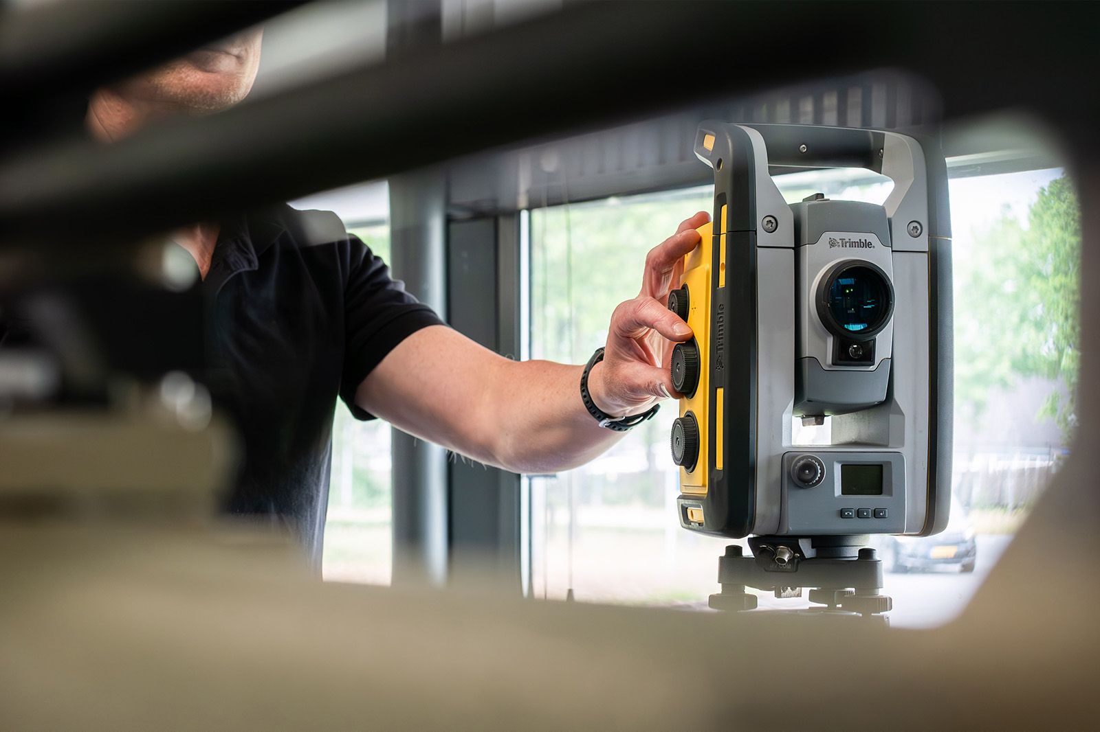 Een close-up van een persoon die een professioneel Trimble landmeetinstrument (total station) bedient.
