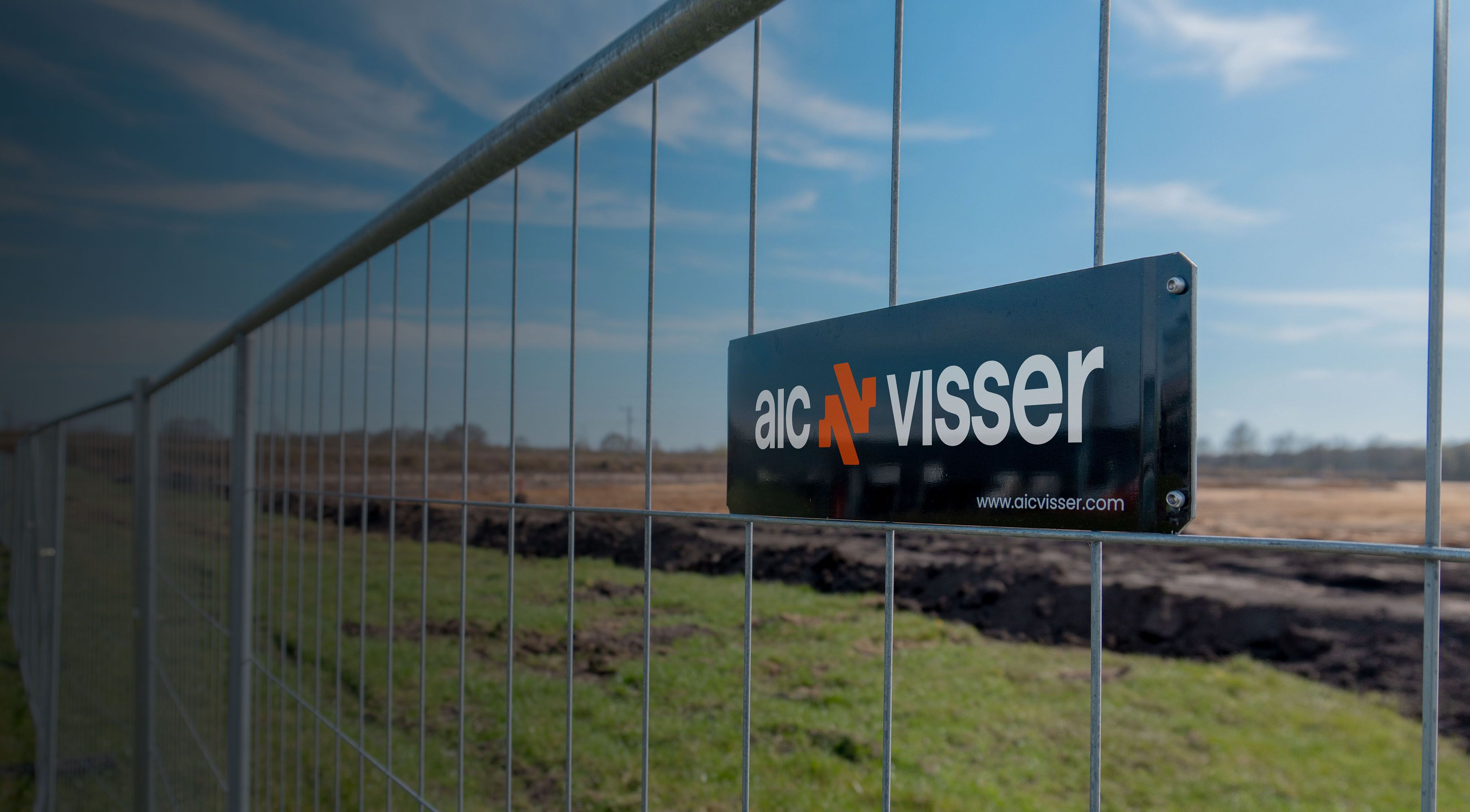 Bouwhek met een zwart bord met de tekst ‘aic visser’ in een open veld.