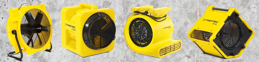 Vergelijking van verschillende bouwventilatoren: axiale en radiale ventilatoren van het merk Trotec in felgele behuizing, opgesteld tegen een betonnen achtergrond.