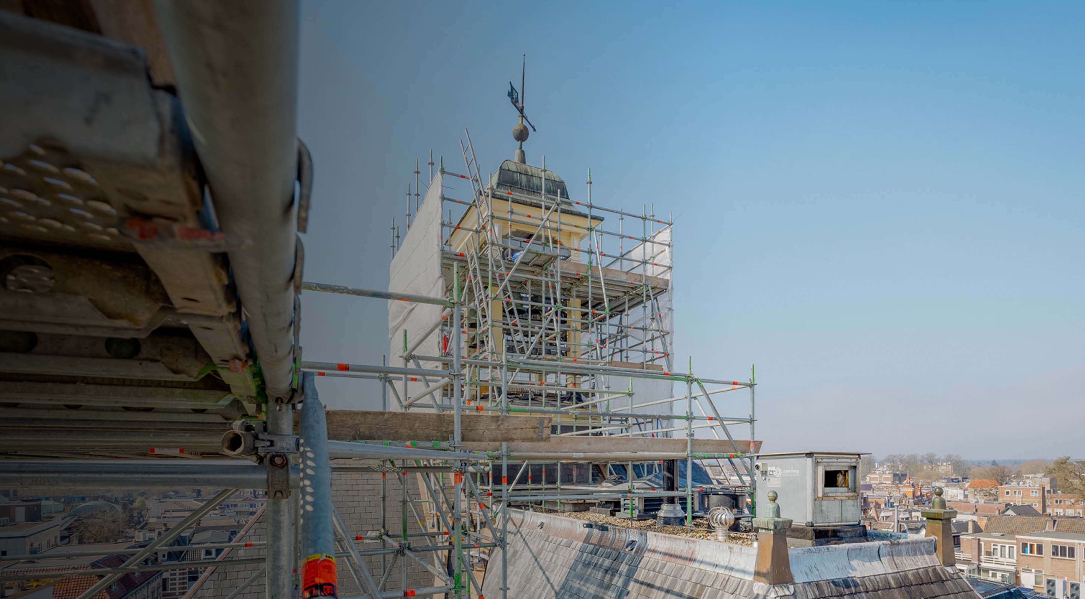 Steigerconstructie rondom een toren op een hoog dak met uitzicht over de stad.