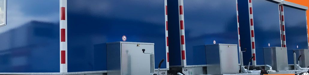 Rij blauwe schaftketen met rood-witte reflecterende strepen, opgesteld naast een oranje gebouw.