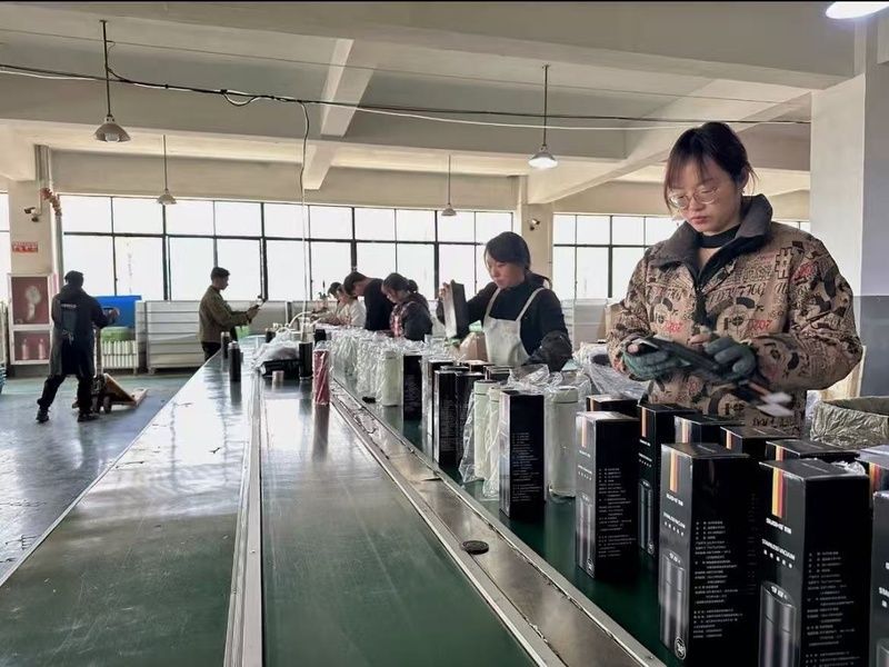 Factory packing line with workers inspecting and packaging stainless steel bottles