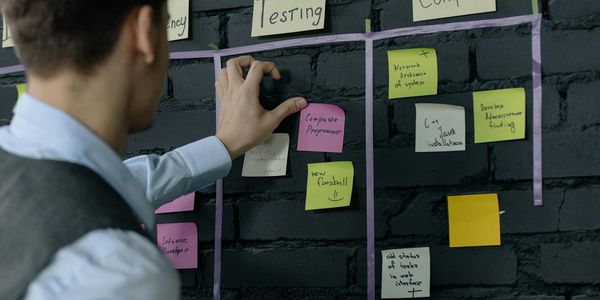 Man organizing project tasks on a wall using sticky notes in a modern office setting.