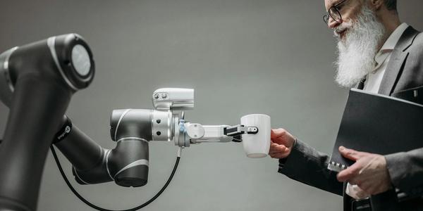 An elderly man receives a cup from a robotic arm in a modern office setting.