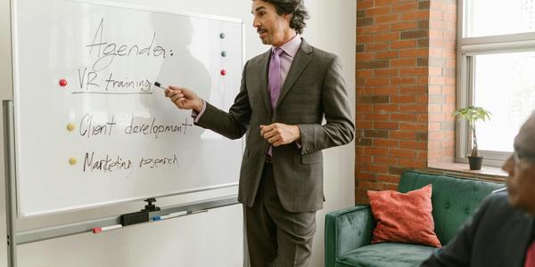 Businessman presenting a whiteboard agenda on VR training in modern office meeting.
