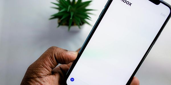 A close-up view of a smartphone screen displaying the email inbox, held by an adult's hand.