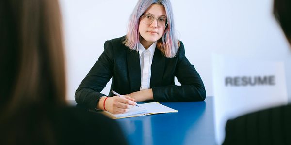 A young woman with dyed hair takes notes during a job interview.