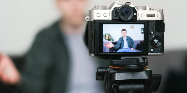 Man recording a vlog indoors using a mirrorless camera on a tripod with selective focus.