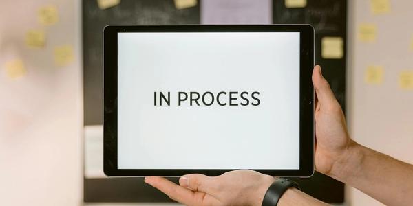 Close-up of hands holding a tablet displaying 'In Process' text, emphasizing workflow.