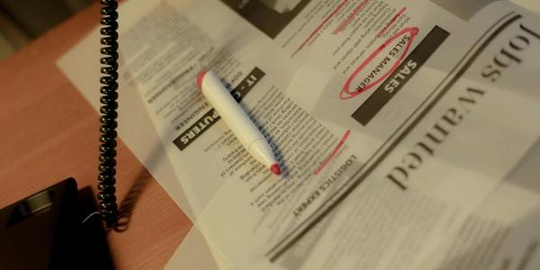 Close-up of a newspaper job section with a red marker and corded phone on a table.