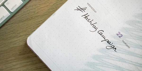 Open planner with 'Hashtag Campaign' handwritten next to keyboard. Ideal for social media and productivity themes.