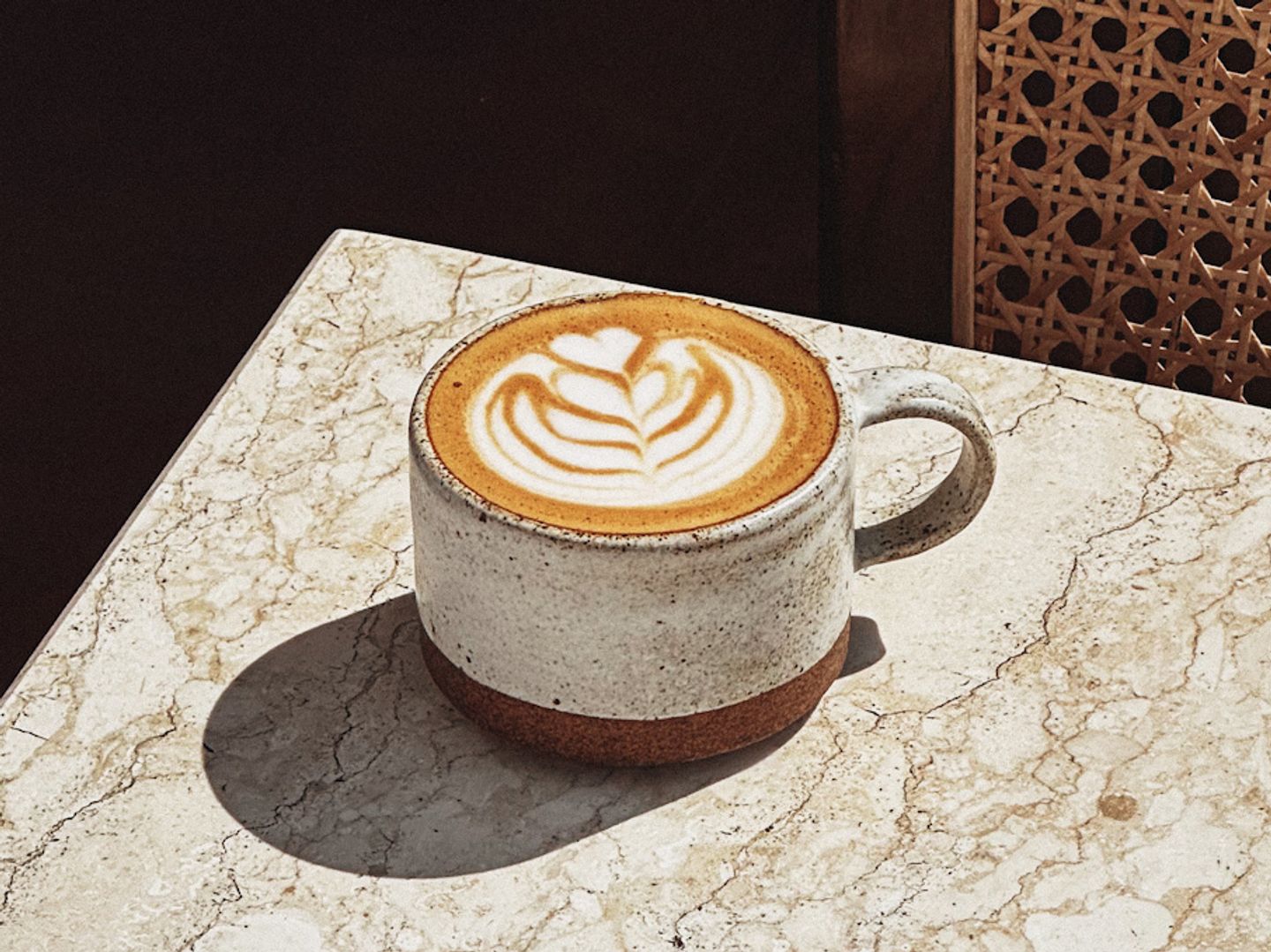 Cappuccino with leaf latte art in a speckled ceramic mug on a marble table.