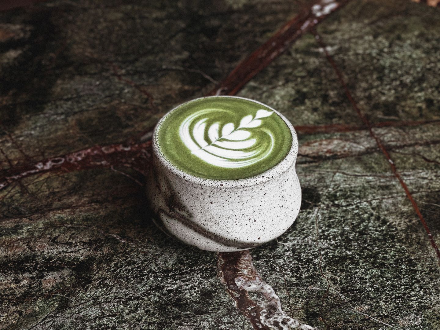 Matcha latte with leaf latte art in a speckled ceramic cup on green marble.