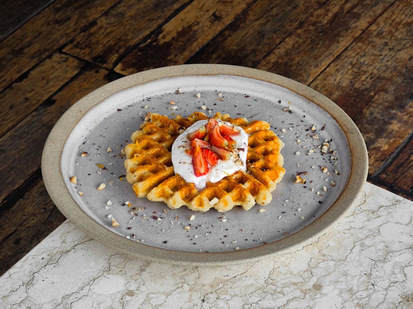 Waffle topped with cream and fresh strawberries, scattered with crushed nuts.
