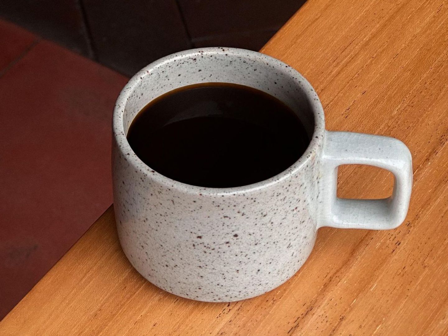 Black coffee in a speckled ceramic mug on a wooden table.