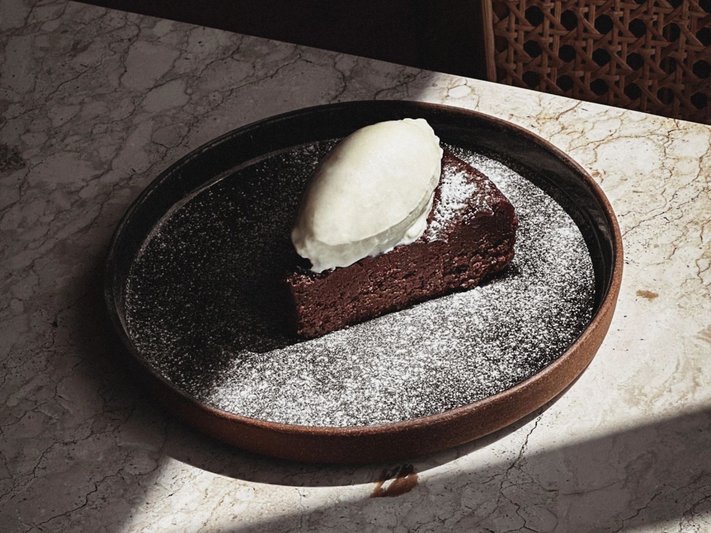 Wedge of dark chocolate cake dusted with icing sugar, topped with a quenelle of vanilla whipped cream.