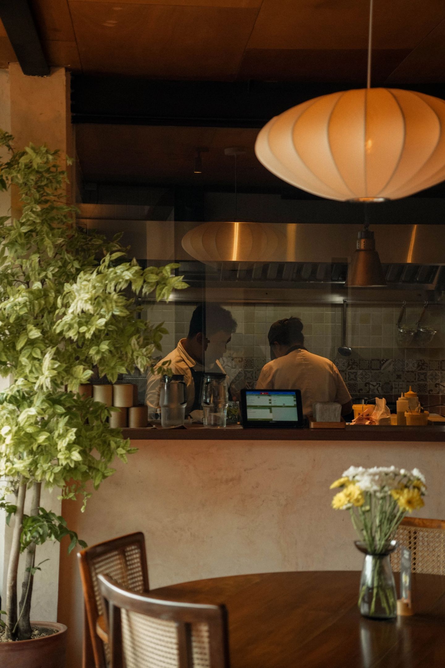 Open kitchen behind glass at House of Sunday, Batu Bolong, with warm pendant lighting and greenery
