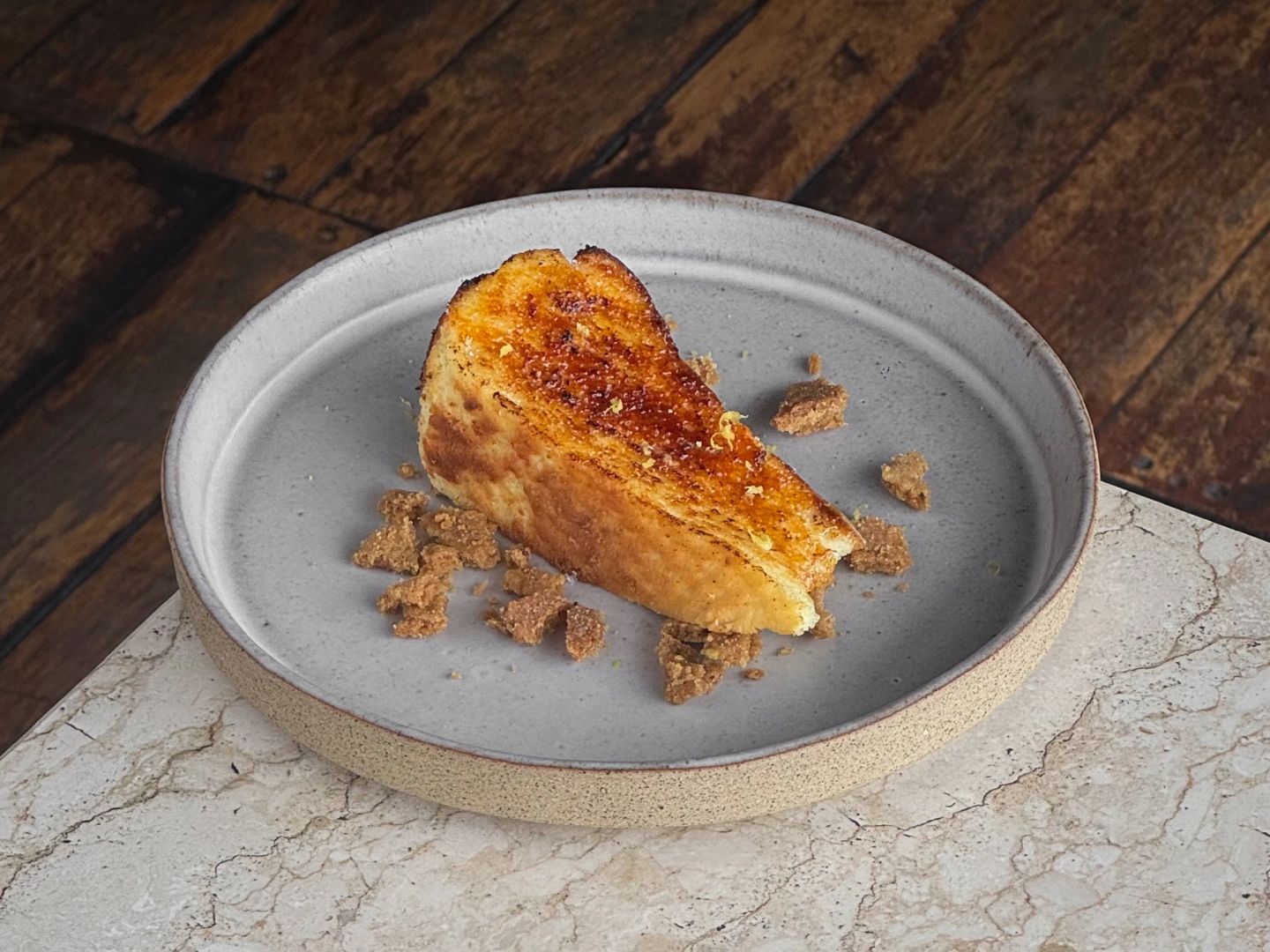 Slice of cheesecake with a torched caramelized top, scattered with crumble.