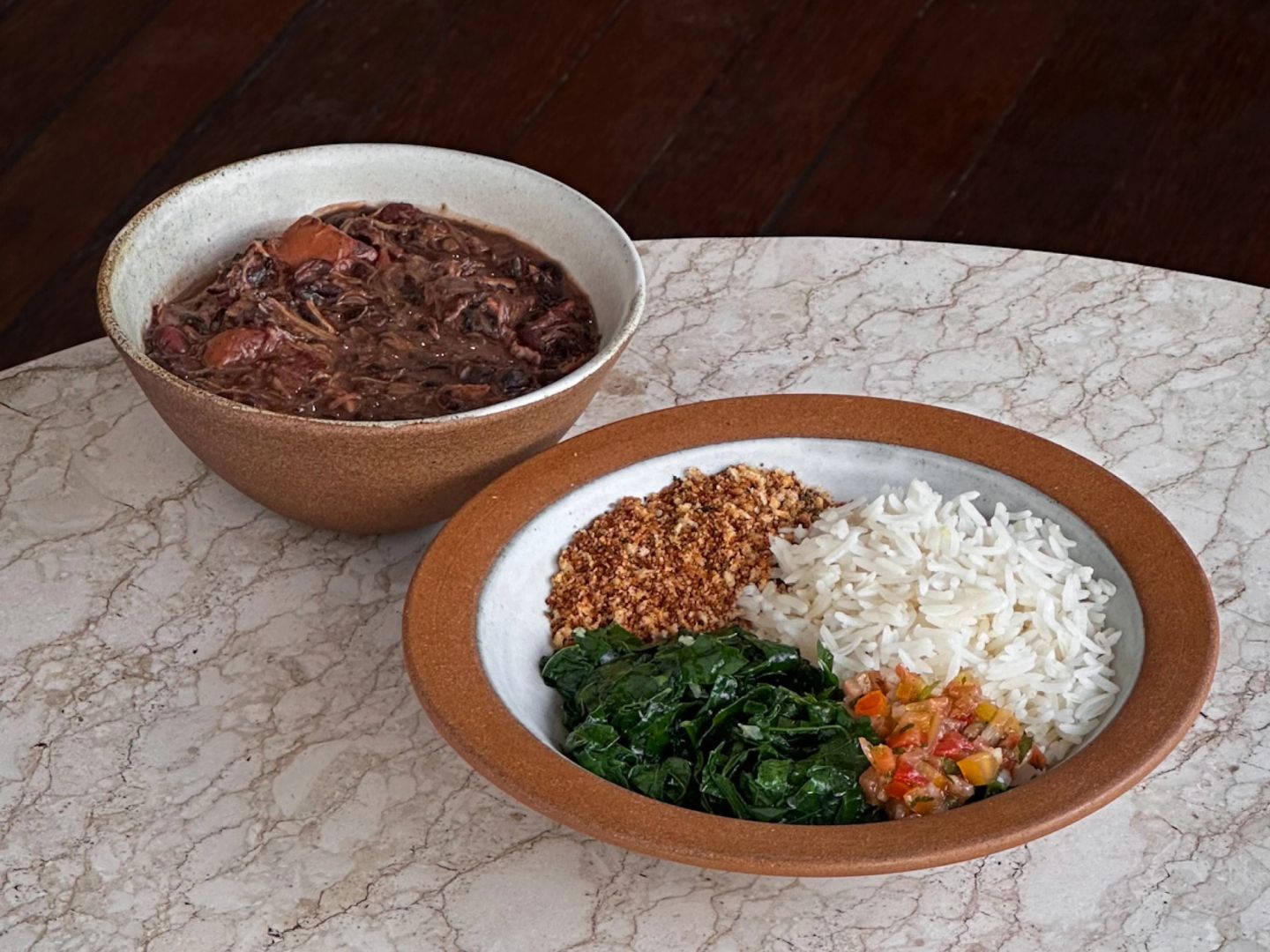 Bowl of feijoada served with rice, sautéed greens, farofa, and salsa on the side.