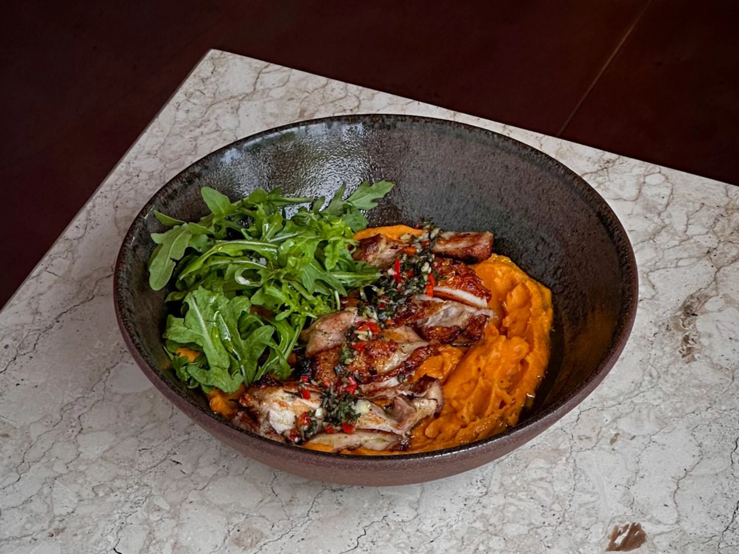 Sliced roast chicken with herb-chilli salsa over sweet potato mash, with a side of rocket.
