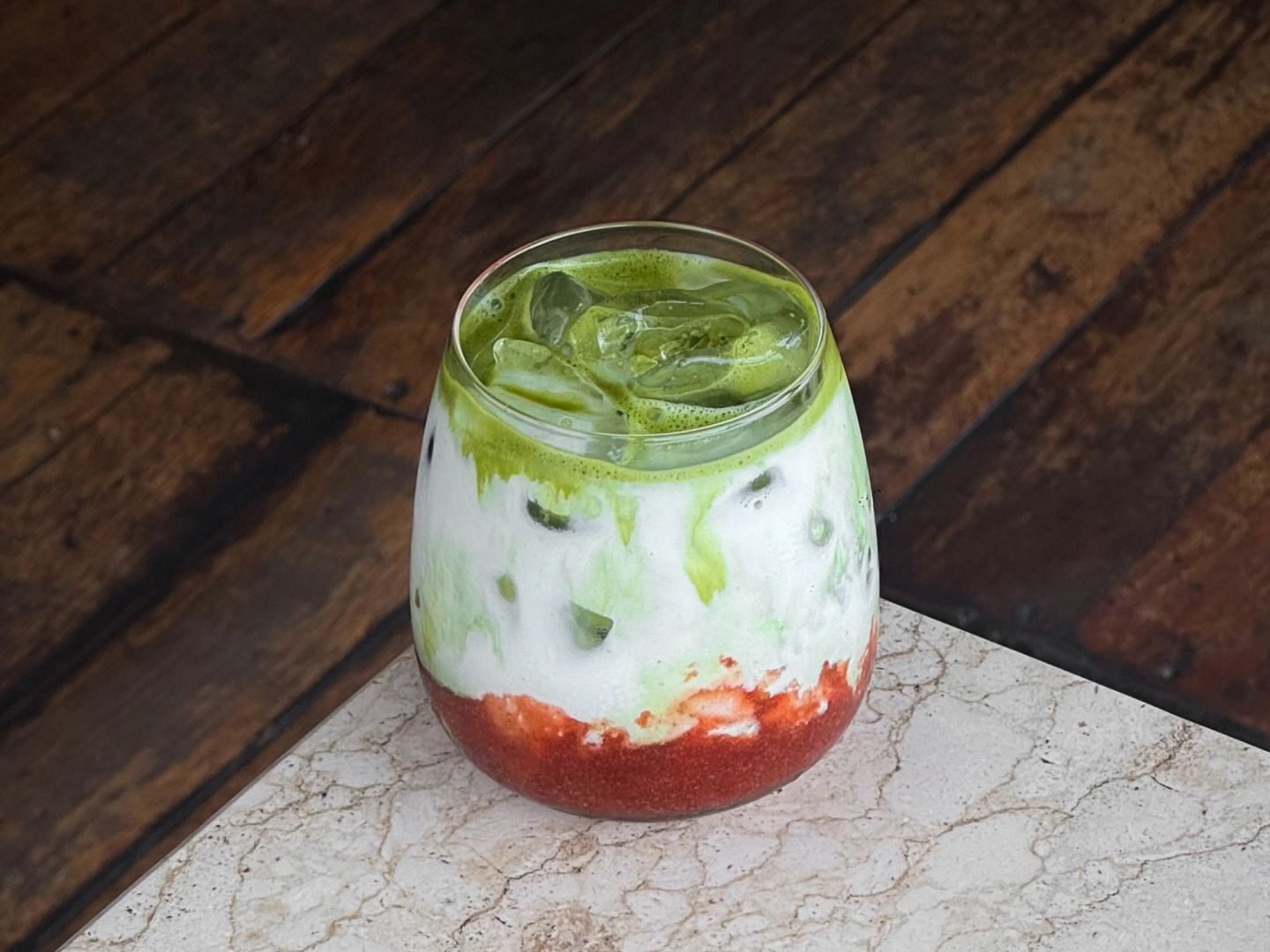 Layered iced drink with homemade strawberry jam, milk, and matcha over ice in a glass.